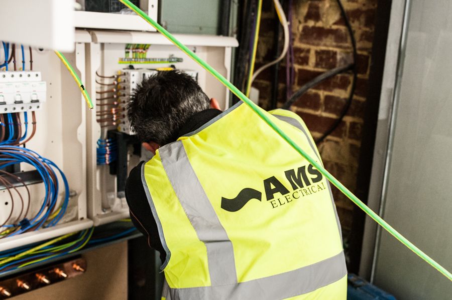 A man facing away from the camera working on electrics within a cable box